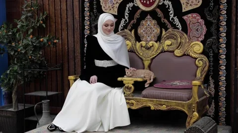 Lady in Arabic clothes with red cat sits on beautiful throne Stock Footage 130642972
