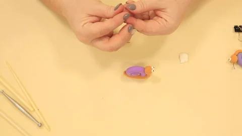 Lady attaches tiny black tendrils to snail from soft polymer clay at beige table Stock Footage 194135484