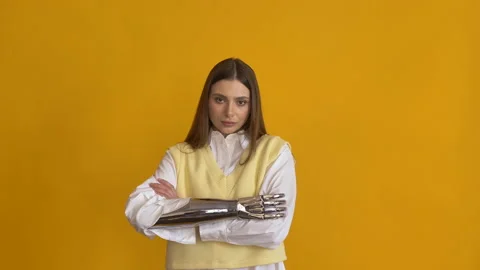 Lady with bionic arm in shirt crosses arms at yellow wall Stock Footage 150240245