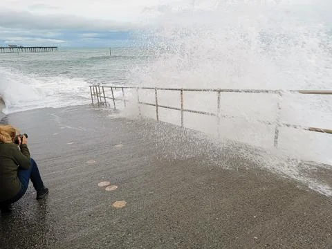 A lady with a camera takes a dramatic stormy sea picture Stock Photos