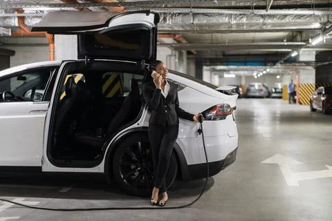 Lady chatting via gadget while charging e-car in parking Stockfoto's