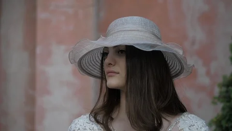 Lady in designed hat and white lacy dress looks around Stock Footage 126605817