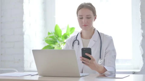 Lady Doctor using Smartphone while using Laptop in Clinic Stock Footage 205001183
