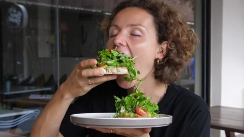 Lady eating with hands big healthy avocado toast with green salad and cherry Stock Footage 166329962