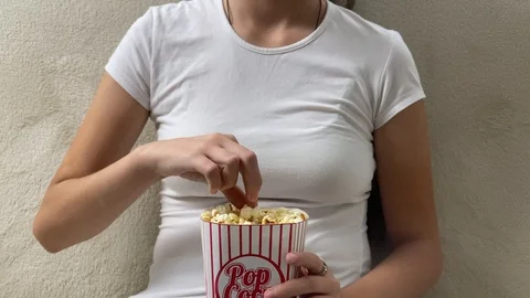 Lady eating popcorn while looking at TV screen Stock Footage 120464739