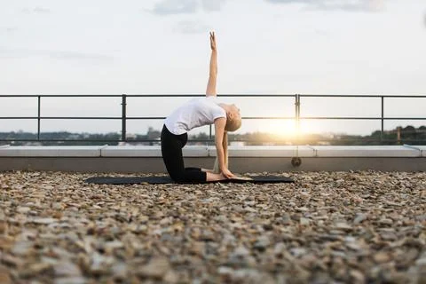 Lady exercising back-bend pose while kneeling on gravel roof Stock Photos
