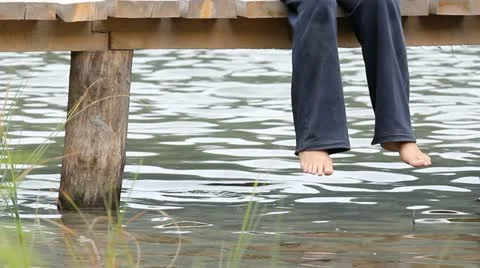 Lady feet hanging on a mountain lake wooden pontoon Stock Footage