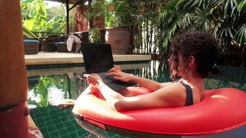Lady is floating in swimming pool on rubber ring and typing on laptop with empty Stock Footage 228580776