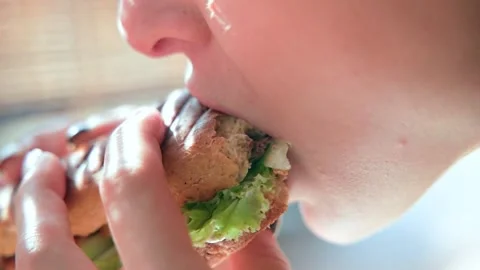 The lady gladly eats a juicy burger with tuna and fresh vegetables. Video stock 234020579