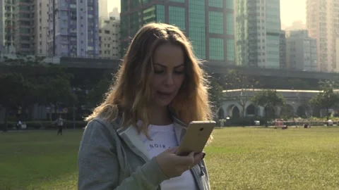 Lady in grey jacket texts message on cellphone in city park Video stock 142032285