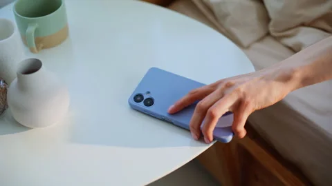Lady hand taking cellphone from bedside table at early wake up bedroom closeup Stock Footage 332703139