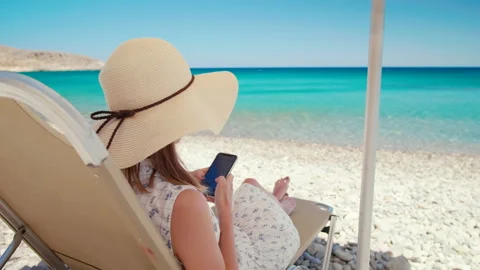Lady in Hat Lying Uses Smartphone on Beach by Sea in Crete, Grece Stock Footage 155409972