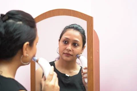 A lady in her 30s using vacuum skin sucker cleaner in front of a mirror as a  Stock-Fotos