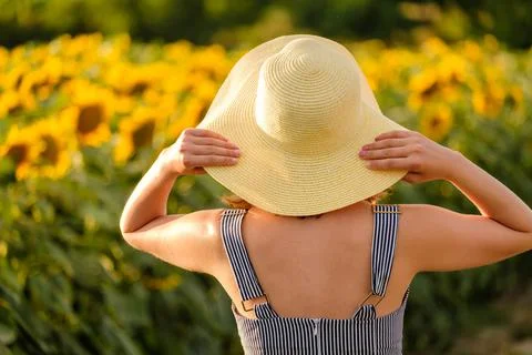 Lady holds straw hat with hands looking at sunflowers Stock Photos