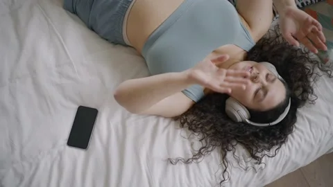 Lady listens to music using wireless headphones lying on bed Stock Footage 163371594
