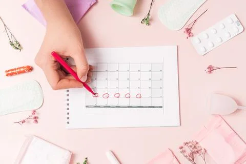 Lady marks with red felt-tip pen in the calendar the menstrual cycle on pink Stock Photos