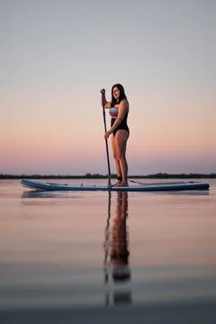 Lady of middle age standing on puddle board smiling rowing with puddle on lake Stock Photos