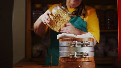 Lady pours raw pine nuts into oil extractor on wooden table Stock Footage 122273381