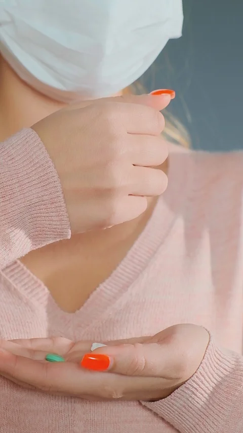 Lady in pullover and white mask throws various pills in hand Stockbeeldmateriaal 127960119