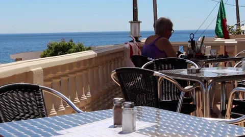 A lady relaxes in a hillside bar overlooking the Atlantic ocean. Stock Footage 64809685