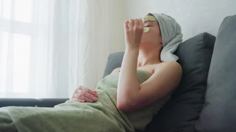 Lady Relaxing on Couch with Cucumber Slice on Face Removing and Eating Enjoying Stock Footage 308593804
