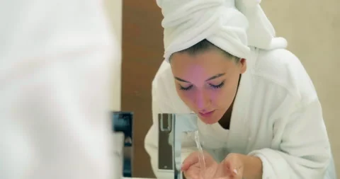Lady in robe washes face looking at large mirror in bathroom Vídeo Stock 141050833