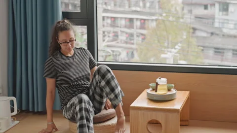 Lady savoring cake by window. Female guest relaxing with beverage and biscuits Stock Footage 337724447