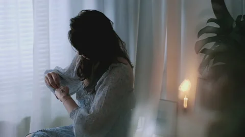 Lady seated next to a bright window putting a bracelet around her wrist Stock Footage 132362525