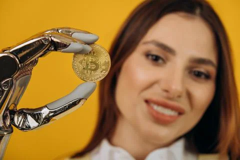 Lady with shiny bionic arm holds golden bitcoin on yellow Stock Photos