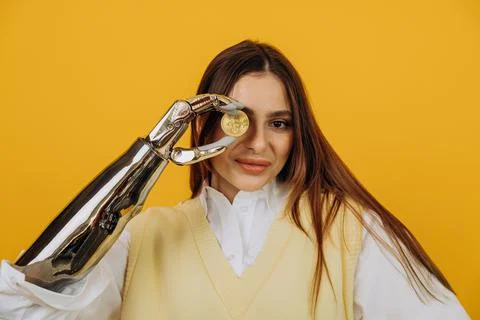 Lady with shiny bionic arm holds golden bitcoin on yellow Stock Photos