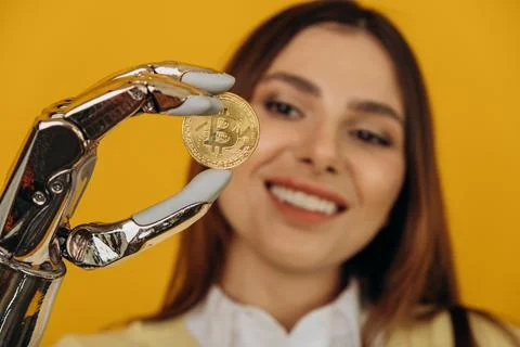 Lady with shiny bionic arm holds golden bitcoin on yellow Stock Photos