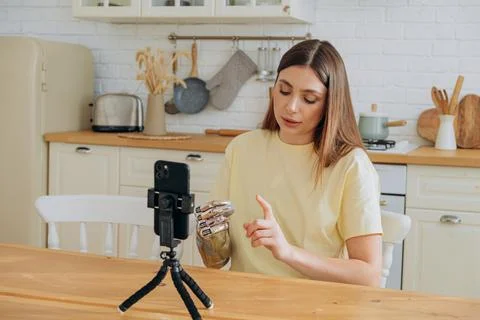 Lady with shiny bionic prosthesis shooting video in kitchen Stock Photos