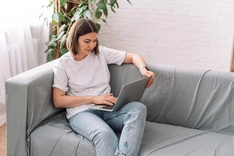 Lady sitting on a gray sofa working on a laptop Stock Photos