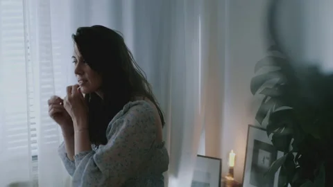 Lady sitting by the window putting on earrings Stock Footage 132361936