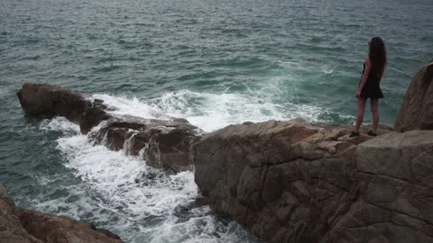 Lady stands on large rock looking at wonderful sea waves Stock Footage 163137933