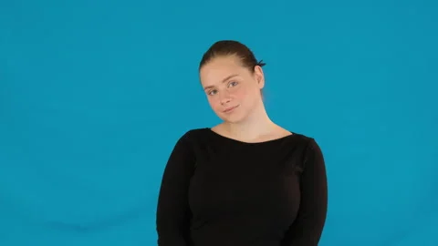 Lady stands looking away showing shyness on blue background Video stock 282912433