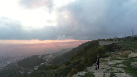 Lady stands on steep slope edge against blue and pink sky Stock Footage 131044894
