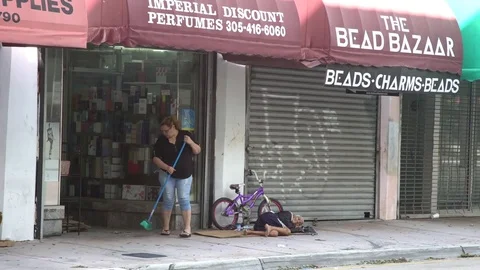 Lady sweeping while a homeless man sleeps on the floor in Florida, USA Stock Footage 81534702