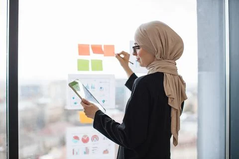 Lady with tablet writing notes on stickers near infographics Stock Photos