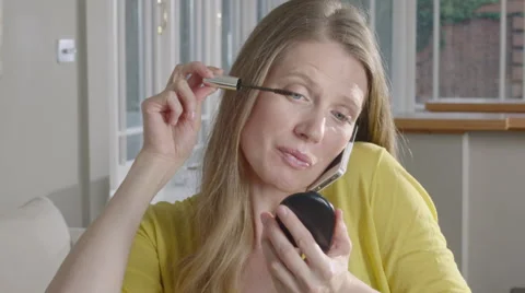 Lady uses mobile Phone while applying make up Stock Footage 63032636