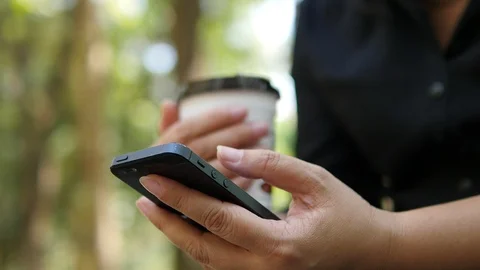 Lady using mobile phone and holding coffee cup over green garden background Video stock 101001636