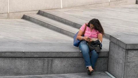 Lady using mobile phone sitting on a parapet near Tower Bridge in London, UK Stock Photos
