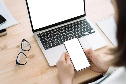 Lady using smartphone in front of laptop with white screen on wooden table Stock Photos