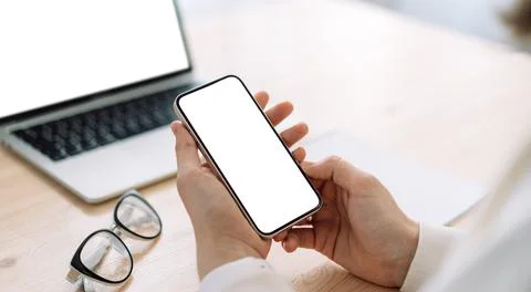 Lady using smartphone in front of laptop with white screen on wooden table Stock Photos