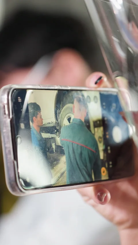 Lady Videos Mechanic at Work Through Smartphone in Workshop Stock Footage 318201546