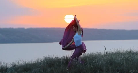 Lady with violet chiffon dances by cam river at sunset light Stock Footage 113673844