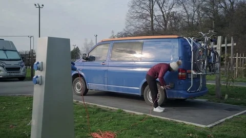 A lady walking to plug in an electrical socket when a blue campervan is Stock Footage 123317256