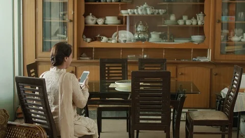 A lady watching her mobile at the dinning table, Back side view of the Stock Footage 104832864