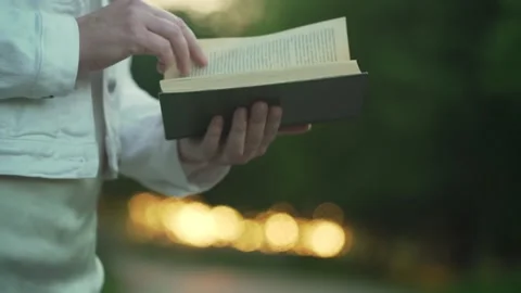 Lady in white denim jacket flips through book pages in park Stock Footage 157471524