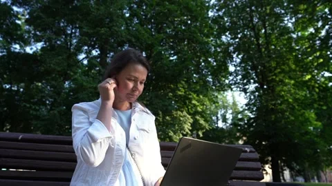 Lady in white looks in computer putting on earphone in park Stock Footage 178550705